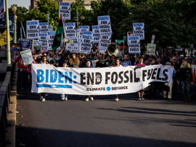 People march behind a banner reading "BIDEN: END FOSSIL FUELS" during an outdoor protest