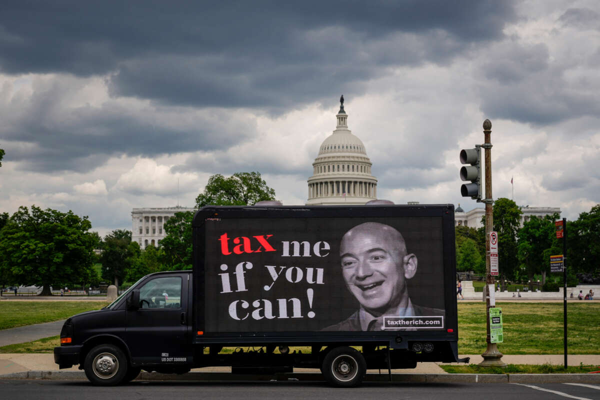 A truck with a digital screen reading "TAX ME IF YOU CAN" beside a photo of Amazon CEO Jeff Bezos drives past the U.S. capitol under a cloudy gray sky