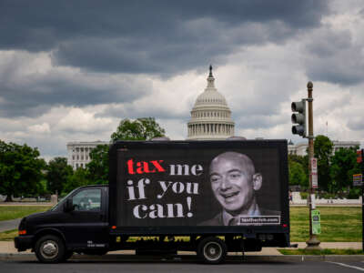 A truck with a digital screen reading "TAX ME IF YOU CAN" beside a photo of Amazon CEO Jeff Bezos drives past the U.S. capitol under a cloudy gray sky