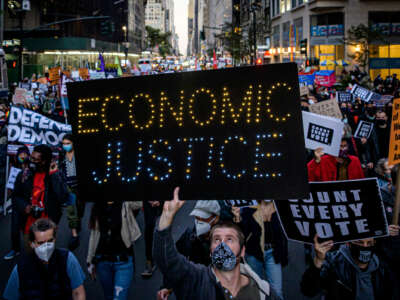 A masked protester holds a lighted sign reading "ECONOMIC JUSTICE" during a protest