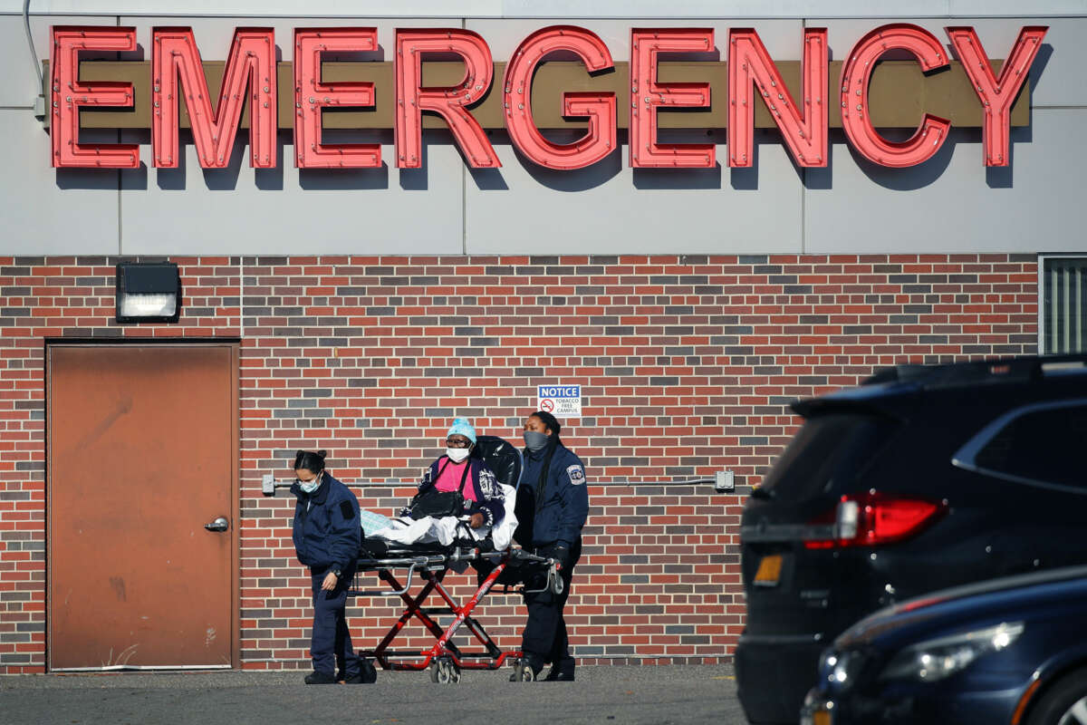 A masked patient is wheeled into the emergency entrance of a hospital by paramedics