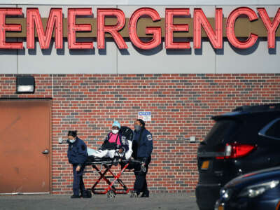 A masked patient is wheeled into the emergency entrance of a hospital by paramedics