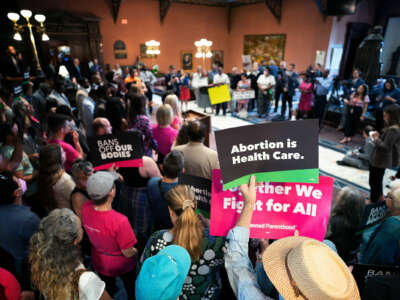 People hold signs reading "BANS OFF OUR BODIES" and "ABORTION IS HEALTHCARE" during a town hall meeting