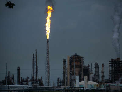 A flare spouting from a petrochemical refinery is seen in against a cloudy sky