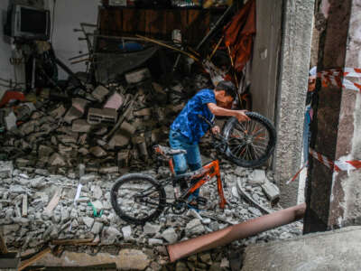 A child pulls his destroyed bike out of rubble that was once an apartment