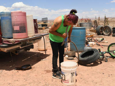 A woman siphons water out of a large plastic barrel