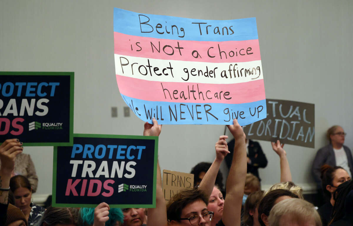 People hold signs during a joint board meeting of the Florida Board of Medicine and the Florida Board of Osteopathic Medicine gather to establish new guidelines limiting gender-affirming care in Florida, on November 4, 2022.