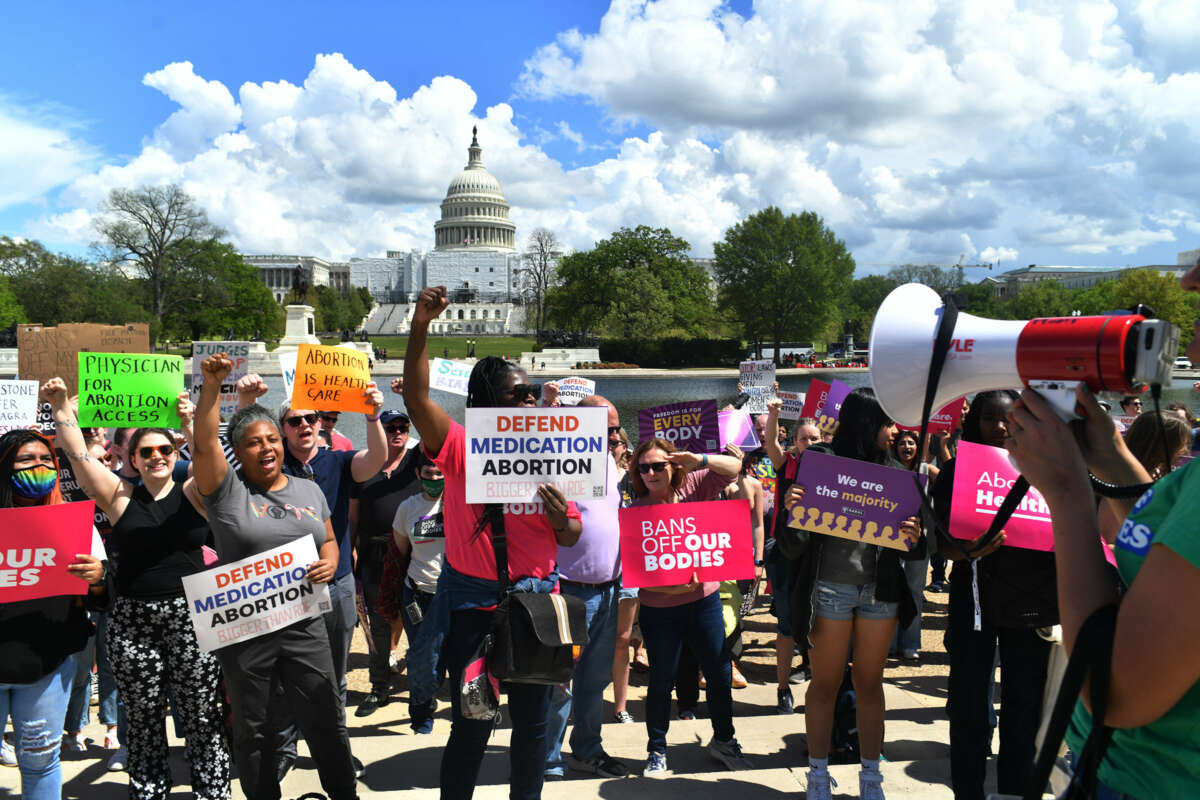 People display signs reading "BANS OFF OUR BODIES" and "DEFEND MEDICATION ABORTION" during an outdoor protest