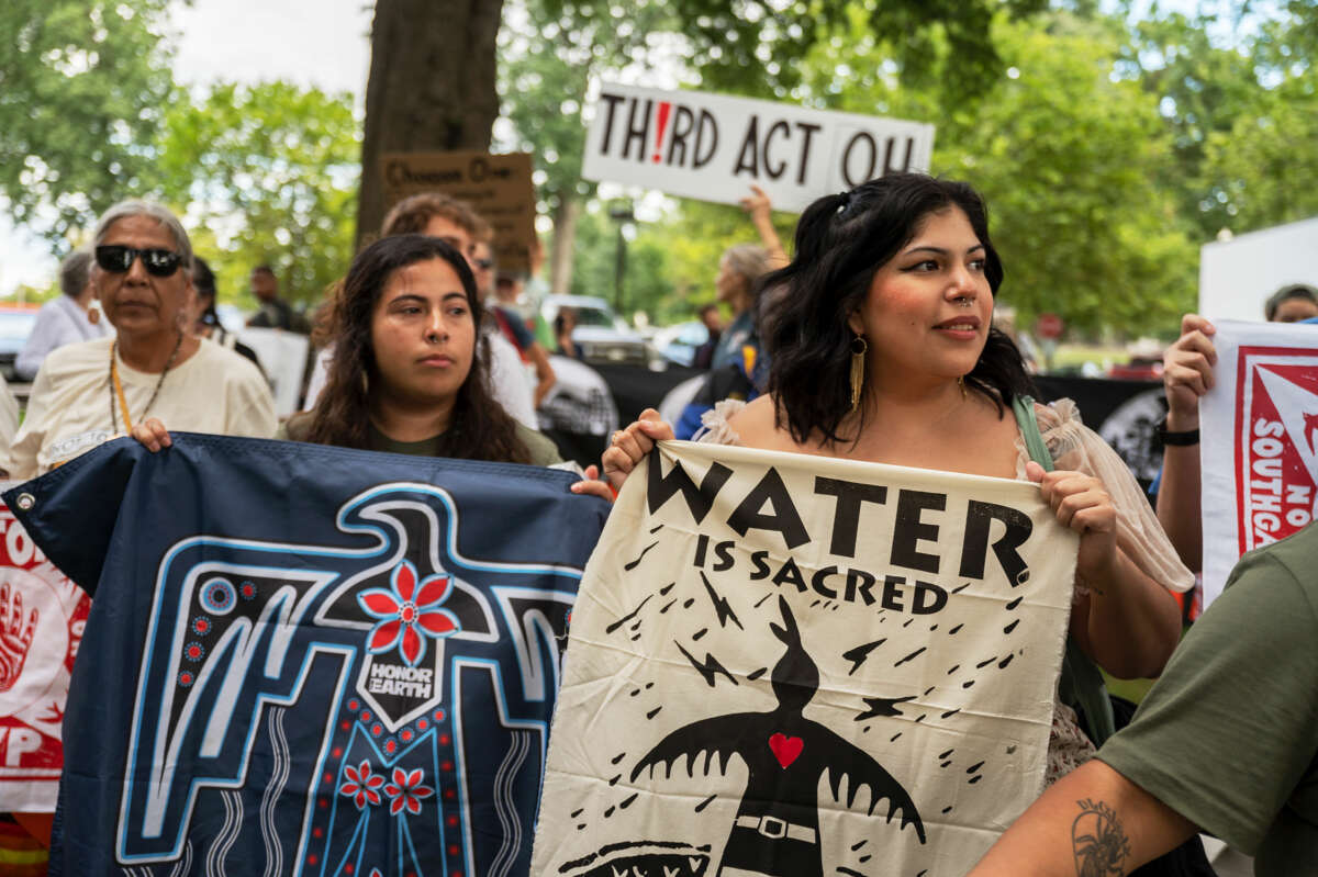 Indigenous protesters display signs reading "WATER IS SACRED" during an outodoor protest
