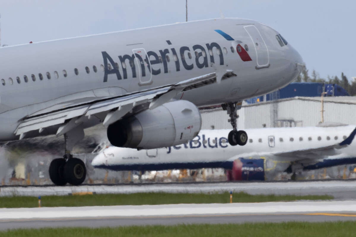 An American Airlines plane lands on a runway near a parked JetBlue plane