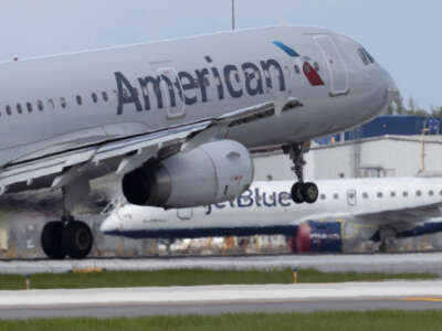 An American Airlines plane lands on a runway near a parked JetBlue plane