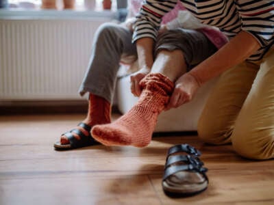 A care worker helps a senior woman put on her shoes and socks