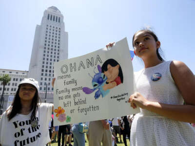A little girl holds a sign reading "Ohana means family, family means nobody gets left behind or forgotten."