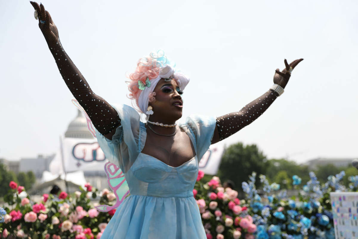 Stormie Dae, dressed in a blue dress with sequined sleeves, greets a crowd with her arms outstretched