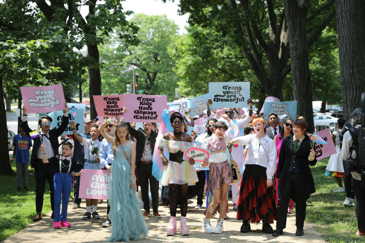 Trans youth, wearing colorful clothing and joyful expressions, march to the capitol holding signs reading "TRANS KIDS HAVE ALWAYS EXISTED" and "TRANS YOUTH ARE POWERFUL"
