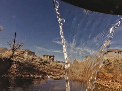 Water flows out of a drainage pipe. Beyond the fall of water, houses and dry land.