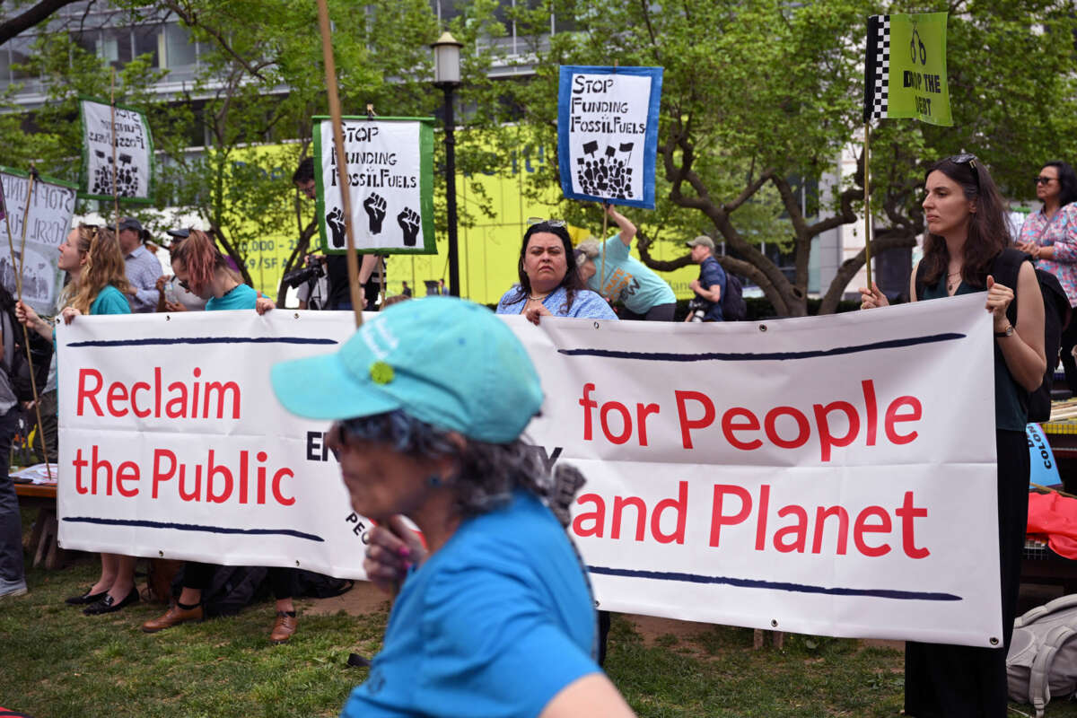People stand behind a banner reading "RECLAIM THE PUBLIC; FOR PEOPLE AND PLANET" during an outdoor protest