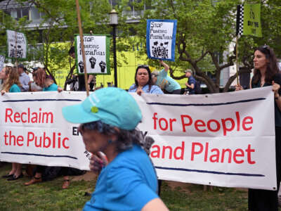 People stand behind a banner reading "RECLAIM THE PUBLIC; FOR PEOPLE AND PLANET" during an outdoor protest