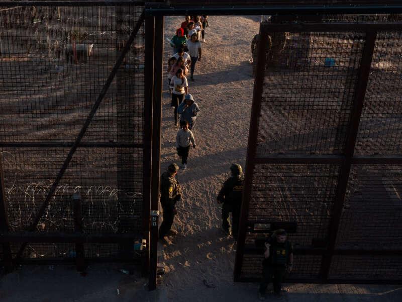 In this aerial picture taken on May 11, 2023, migrants walk through gate 42 to board vans after waiting along the border wall to surrender to U.S. Border Patrol agents for immigration and asylum claim processing upon crossing the Rio Grande river into the United States on the U.S.-Mexico border in El Paso, Texas.