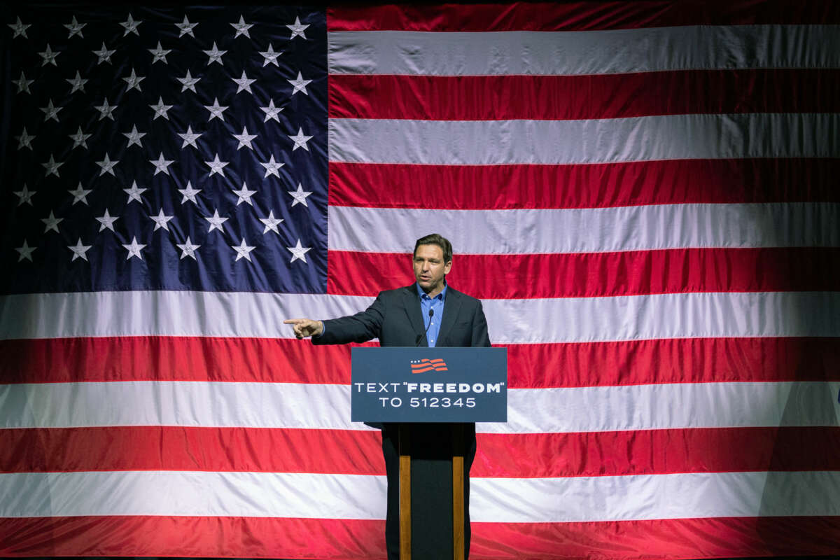 Ron Desantis speaks to a crowd in front of a large, wrinkled us flag