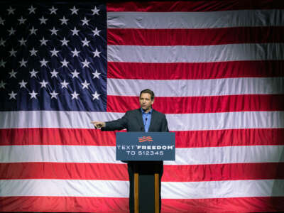 Ron Desantis speaks to a crowd in front of a large, wrinkled us flag