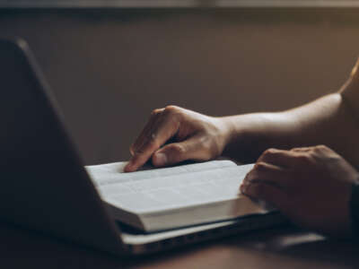 Person looking at book while on laptop