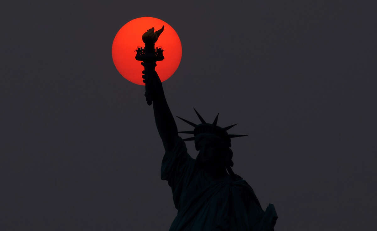 The sun is shrouded as it sets behind the Statue of Liberty in a hazy sky caused by smoke drifting into the Northeast of the U.S. from wildfires in Canada on May 22, 2023, in New York City.