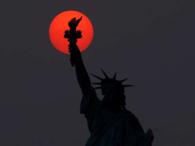 The sun is shrouded as it sets behind the Statue of Liberty in a hazy sky caused by smoke drifting into the Northeast of the U.S. from wildfires in Canada on May 22, 2023, in New York City.