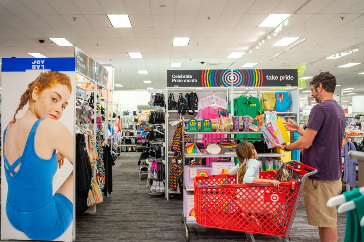 A dad pushes his child in a shopping cart through the Pride section of a Target's clothing department