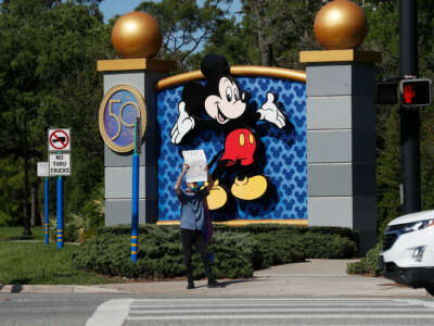 A lone protester standing outside of the Walt Disney World entrance holds a sign reading "TRANS RIGHTS ARE HUMAN RIGHTS"