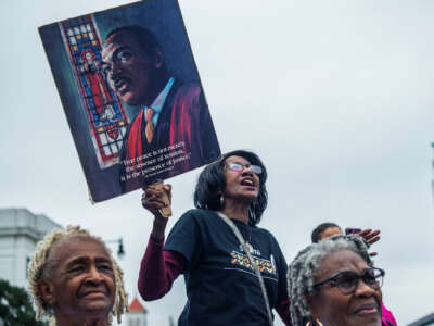 A woman chants alongside other protesters while holding a sign baring Reverend Dr. Martin Luther King's face