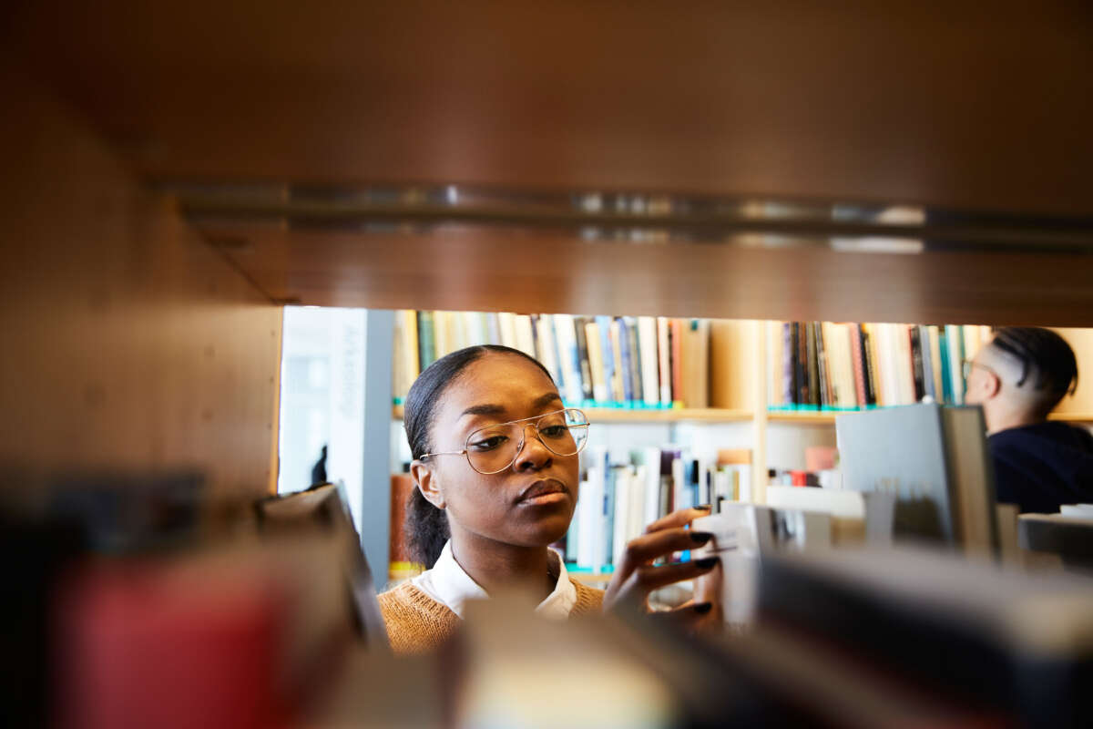 Black student looking at book in library shelf