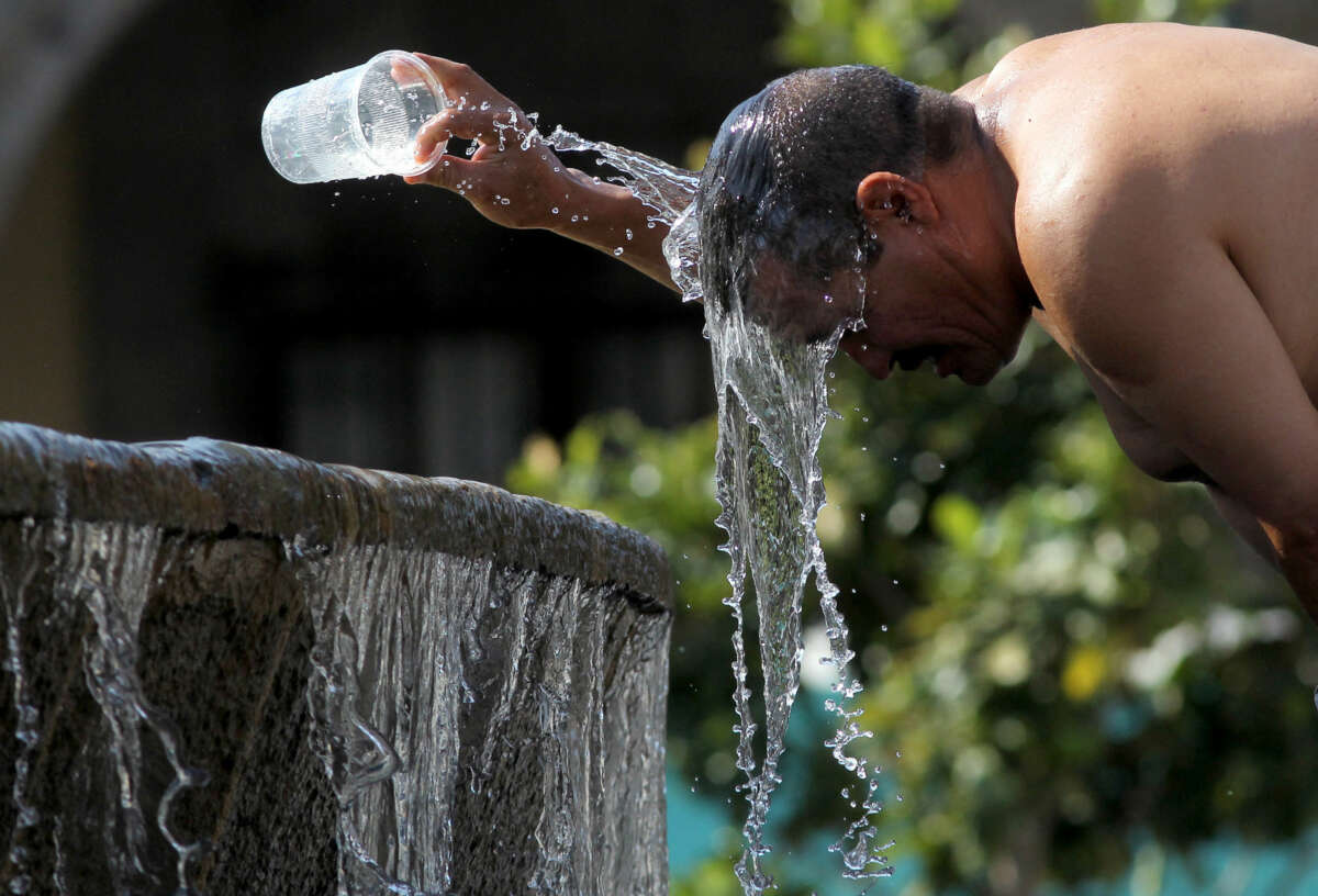 A man splashes water on his head while standing at an outdoor fountain