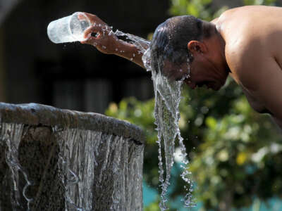 A man splashes water on his head while standing at an outdoor fountain