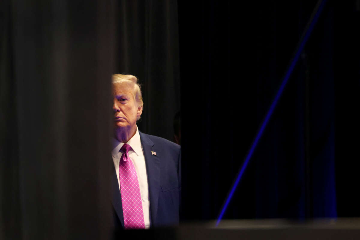 Donald Trump partially obscures himself behind black curtains