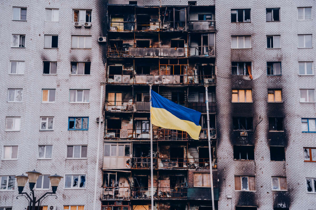 A bombed and burned-out apartment complex is seen behind the Ukrainian flag