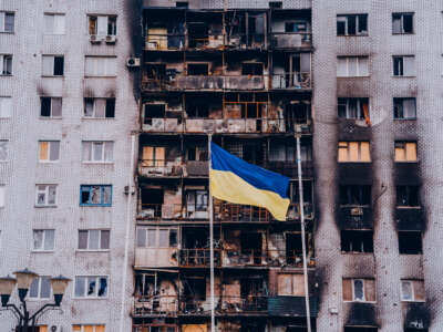 A bombed and burned-out apartment complex is seen behind the Ukrainian flag