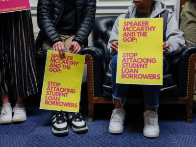 People sit while holding signs reading "SPEAKER MCCARTHY AND THE GOP: STOP ATTACKING STUDENT LOAN BORROWERS"