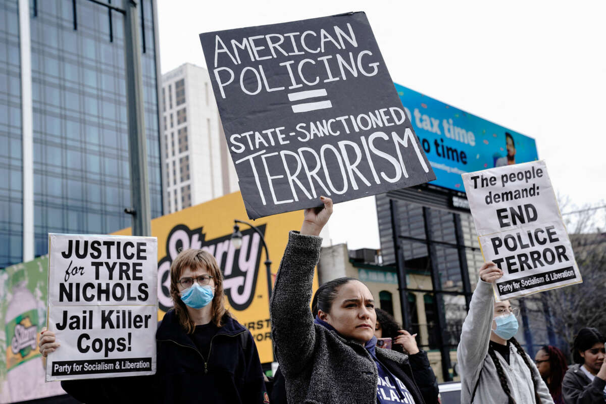 A protester holds a sign reading "AMERICAN POLICING = STATE-SANCTIONED VIOLENCE" during an outdoor protest