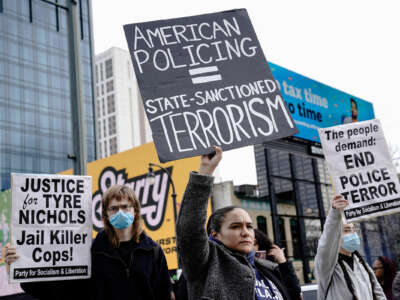 A protester holds a sign reading "AMERICAN POLICING = STATE-SANCTIONED VIOLENCE" during an outdoor protest