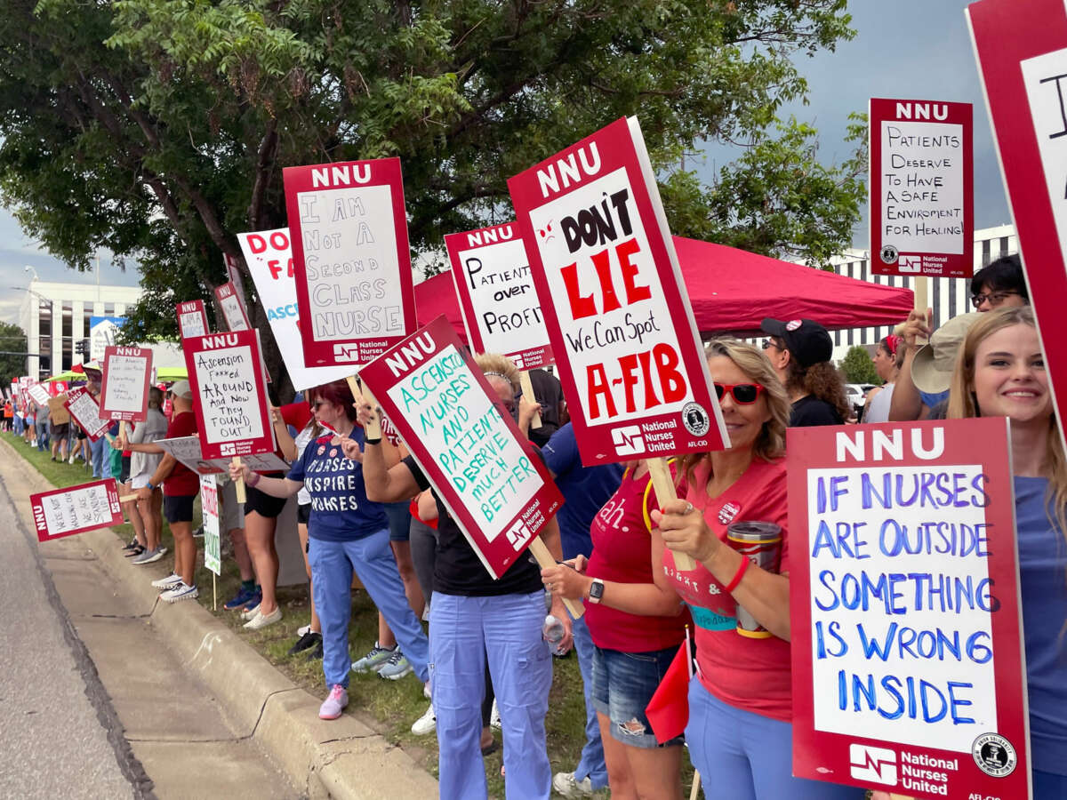 People dressed in red and holding picket signs line a street during an outdoor protest