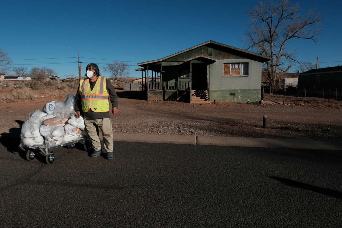 A worker stands next to a dolly loaded with plastic bags filled with food