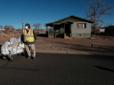 A worker stands next to a dolly loaded with plastic bags filled with food