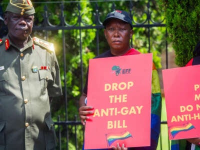 A man holds a sign reading "DROP THE ANTI-GAY BILL" during an outdoor protest