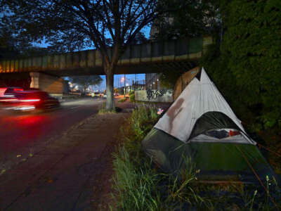 An unhoused person smokes a cigarette at dusk at her new campsite on a spot near a rail bridge overpass on New York Ave. in Washington, D.C., on May 12, 2023.