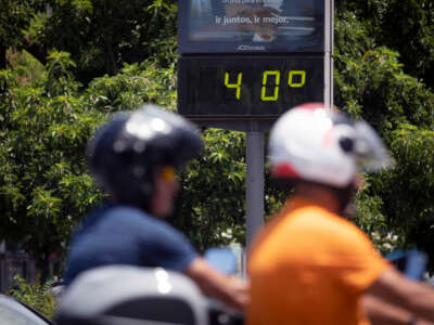 Motorbikers ride past a lit sign displaying the current outdoor temperature of 40ºC, which is roughly 104ºF