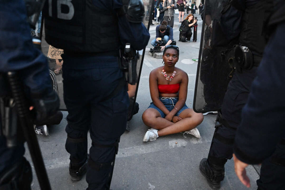 An unarmed Black protester sits on the ground as she's surrounded by French riot police