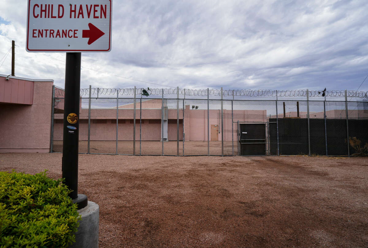 A sign reading "CHILD HAVEN" is seen outside of the razor-wire festooned fence of what is obviously some form of prison