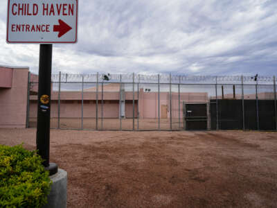 A sign reading "CHILD HAVEN" is seen outside of the razor-wire festooned fence of what is obviously some form of prison