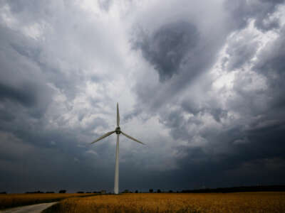 A lone wind turbine stands against cloudy skies